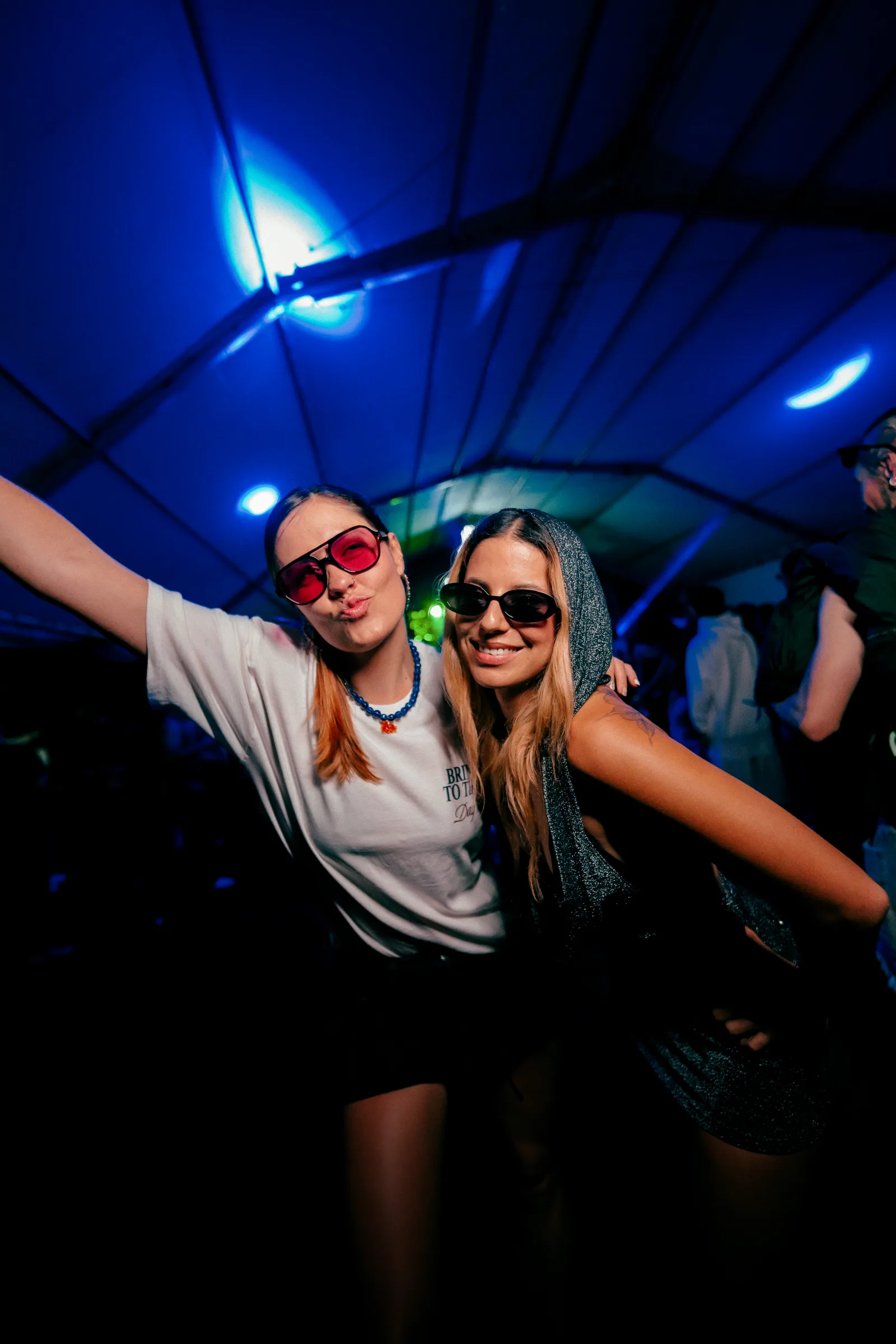 Dos amigas posando con gafas bajo luces azules