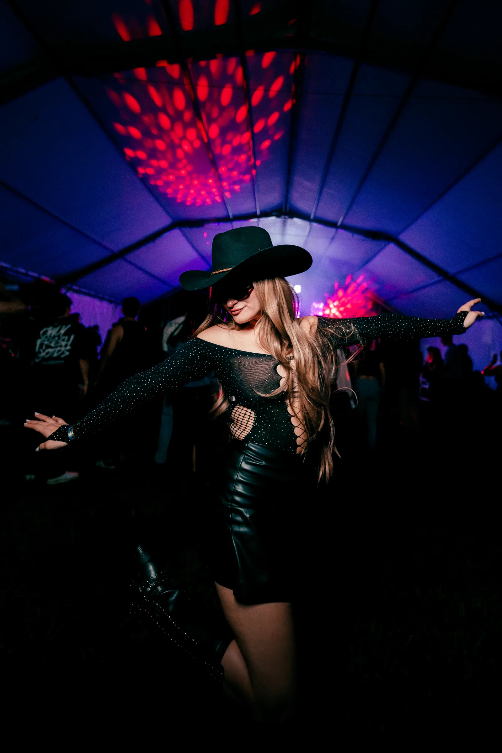 Asistente bailando con sombrero negro bajo luces violetas y rojas